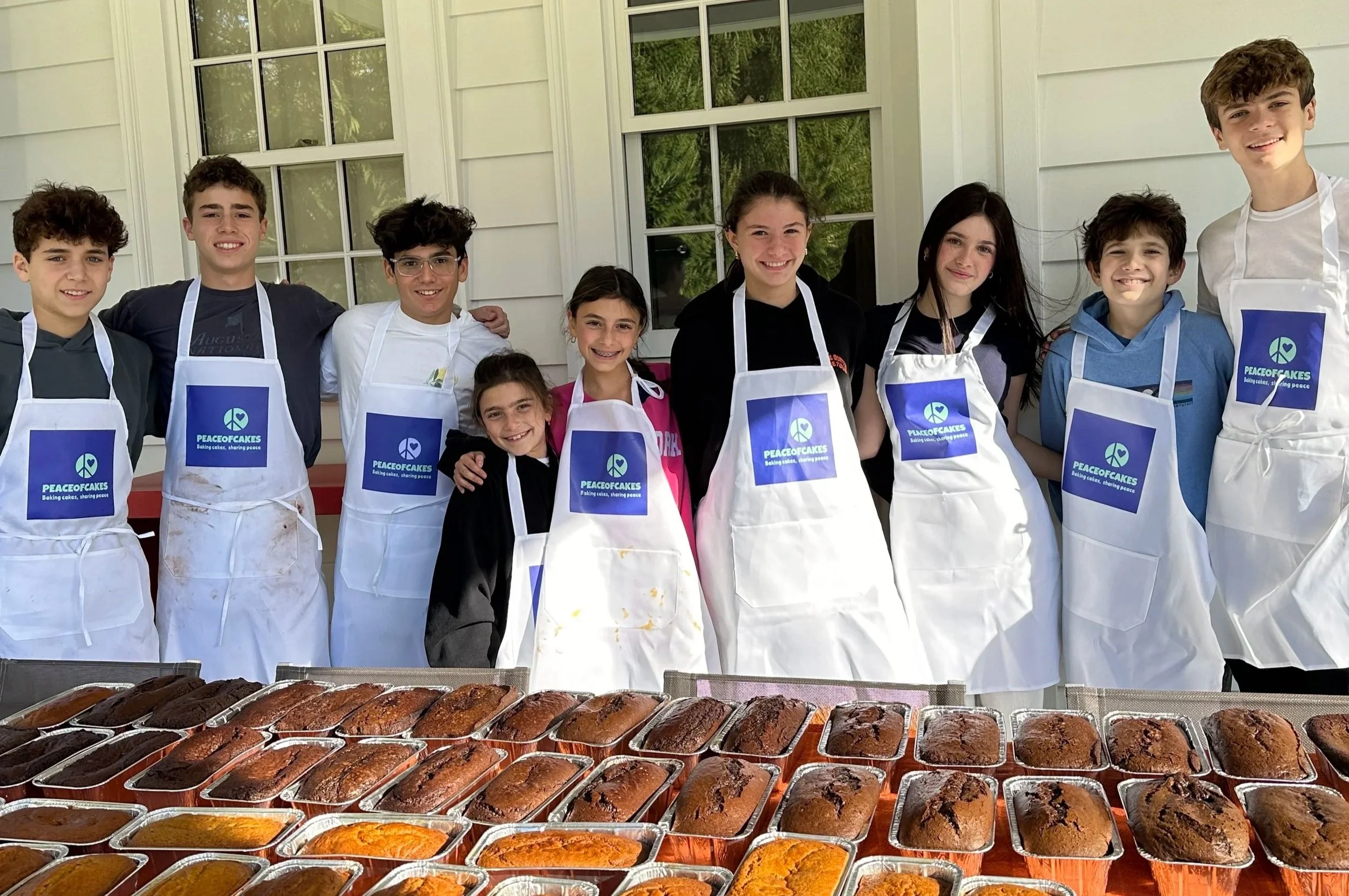 Young PeaceofCakes bakers behind rows of wrapped cakes