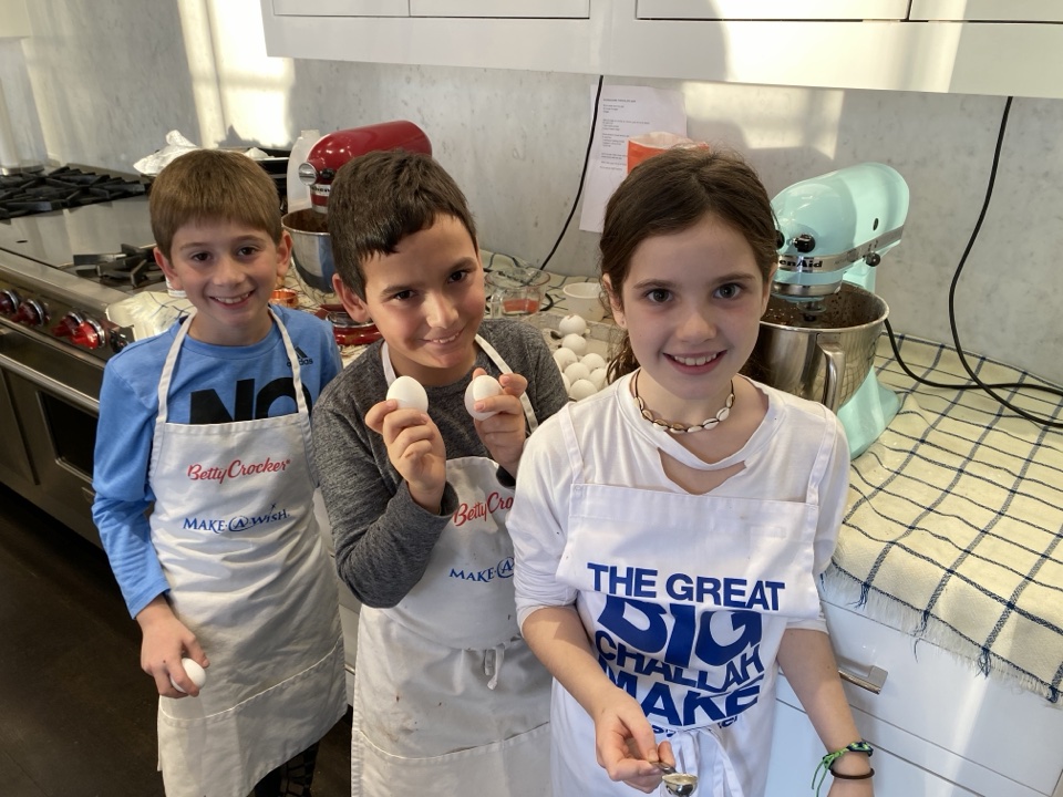 Three young PeaceofCakes bakers in aprons holding eggs beside stand mixers